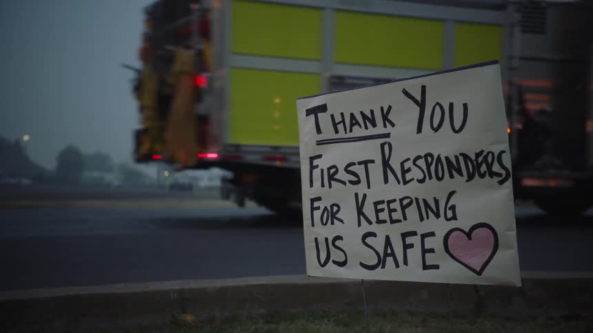 Sign staked by the side of the road thanks first responders as a fire engine and other official vehicles pass