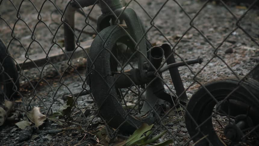 A rusting tricycle sits behind a chain link fence