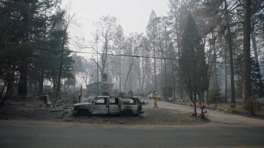 A person in a hazmat suit goes to survey the damage where a vehicle burned in a forest fire