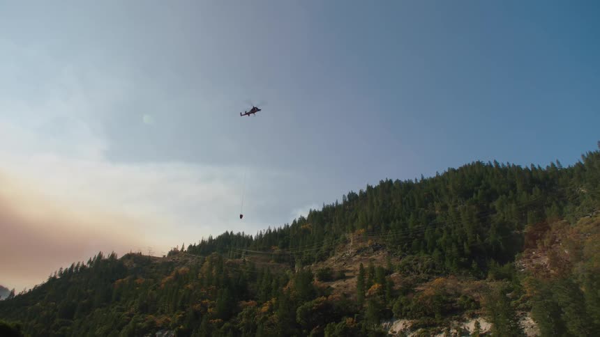 A helicopter flying over a mountain forest then lowering toward a river