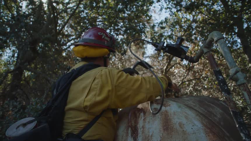 A firefighter adjusts the hose on a tank in the forest