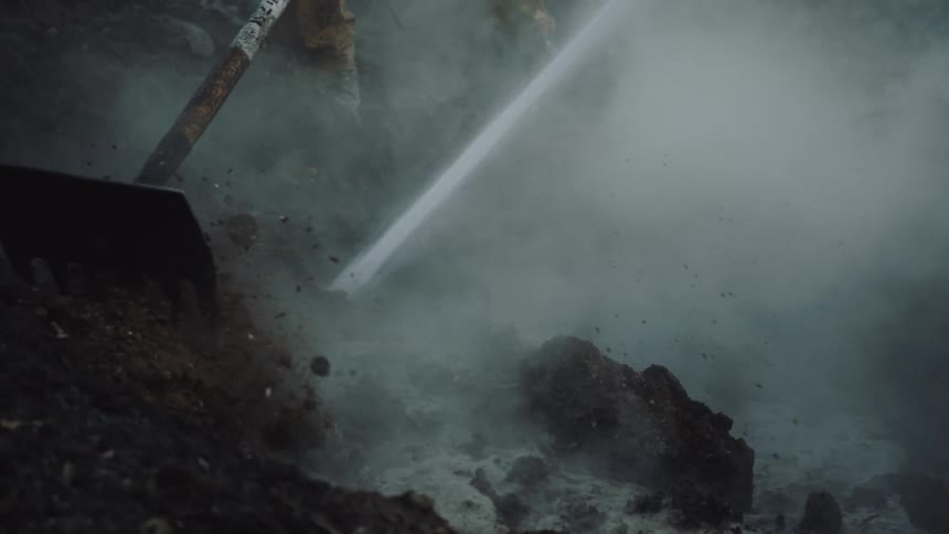 Putting out fire with fire hose and rake in forest with steam coming off