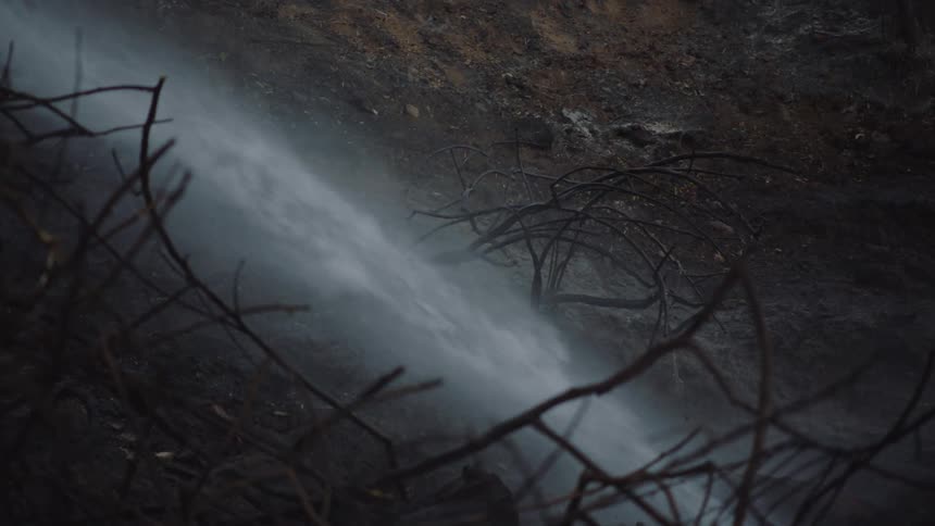 The smoldering ground is being thoroughly soaked with water by a fireman after a fire