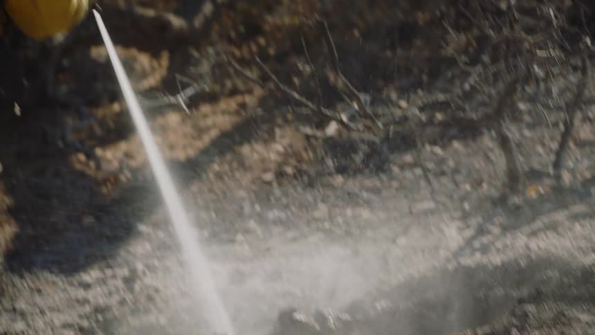 First responder hosing off burning wood in aftermath of a forest fire