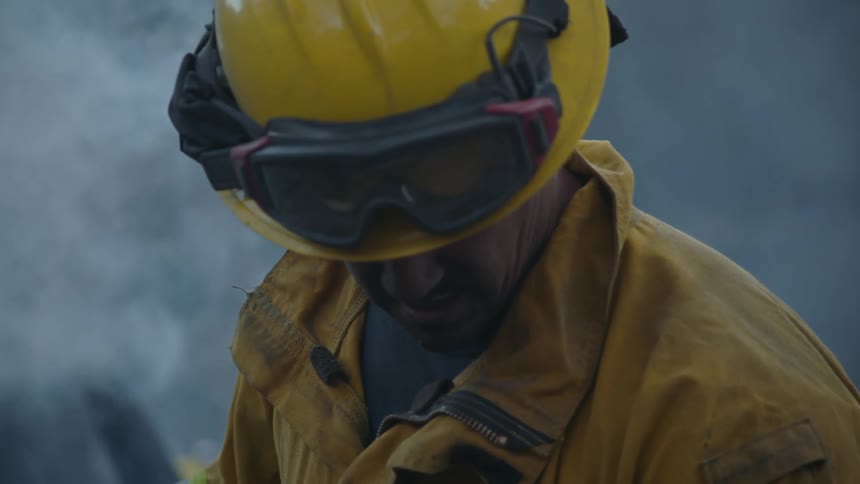 A firefighter is standing outside looking down as smoke fills the air around him
