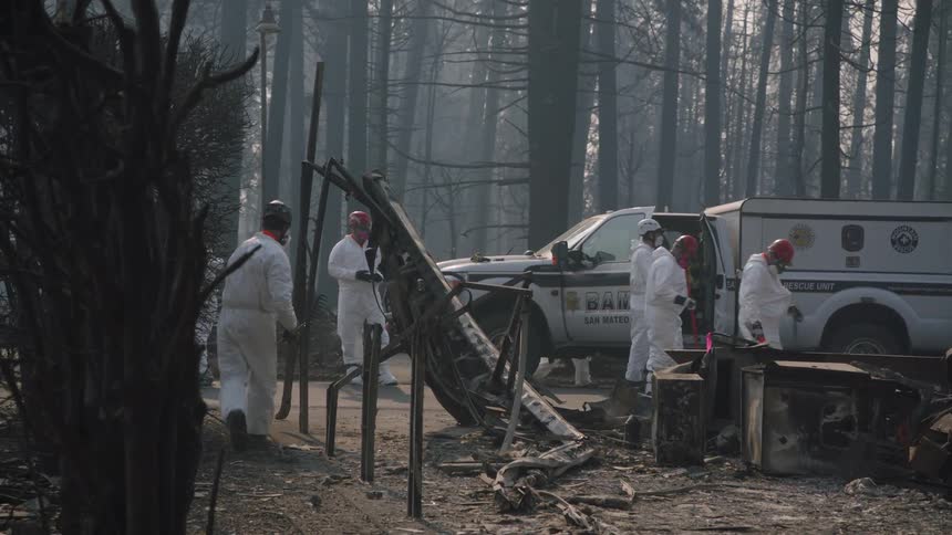 Workers wearing white suits walking around with tools and moving around debris