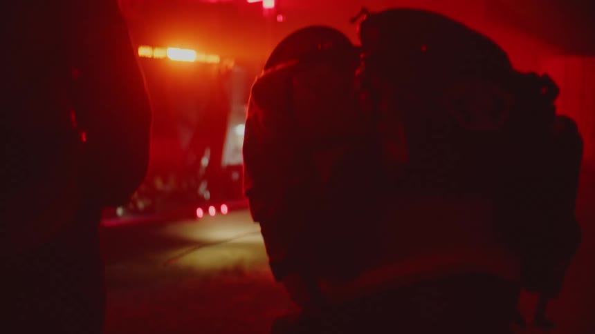 Three silhouettes of firemen standing near a firetruck with flashing lights