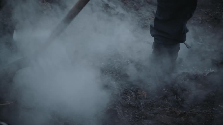 Firefighter digs at smoking ground to deal with remains of wildfire