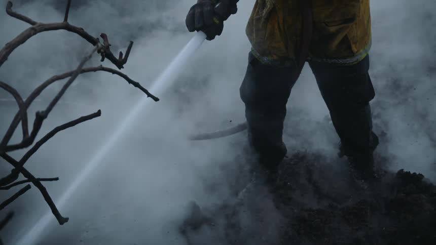 A fireman is using a fire hose to spray the smoldering remains of a forest fire