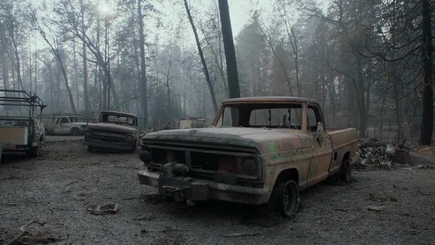 Burned out trucks sit among debris in the woods as smoke fills the air