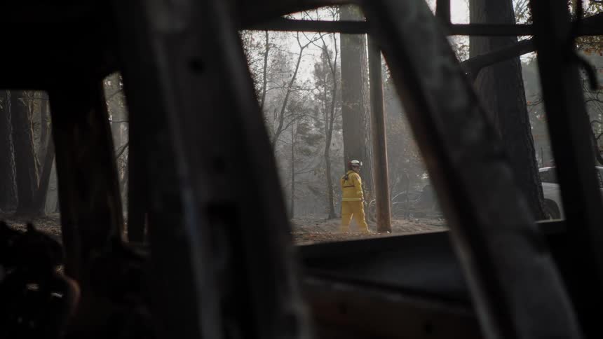 A view through rubble of a firefighter walking through a forest