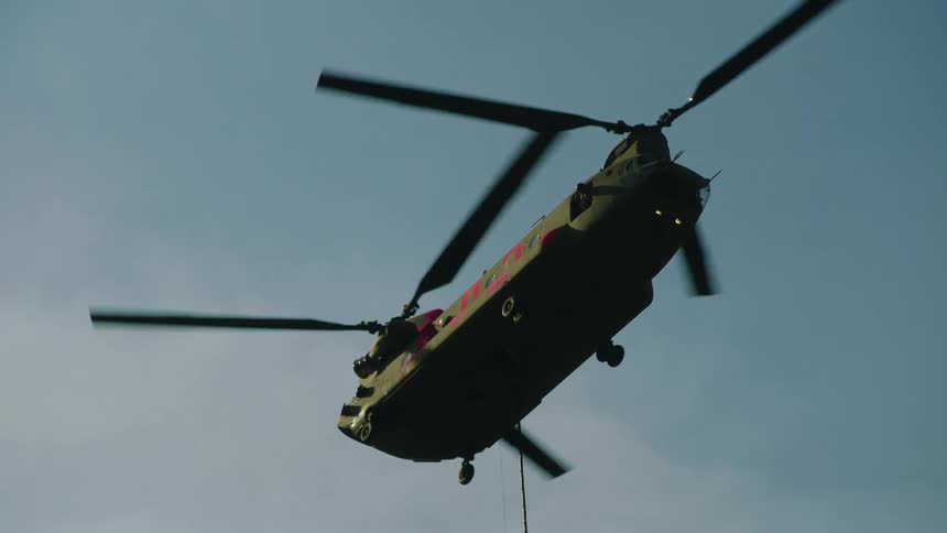 Helicopter rotors turn as they fly in a blue sky and cables hang down below