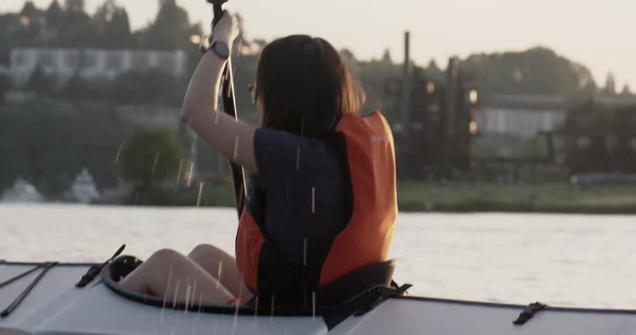 A woman paddles a kayak with a shoreline in view