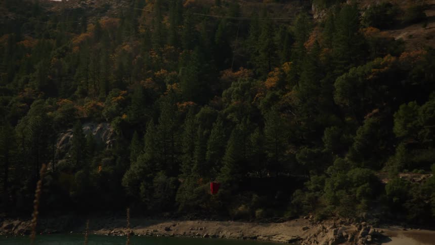 A fire fighting helicopter is dipping a large bucket into a lake to gather water for dumping onto a forest fire in the daytime