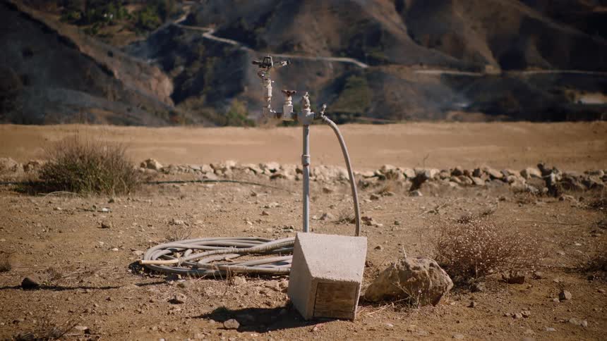 A sprinkler system and spigot with hose attached to it in the desert