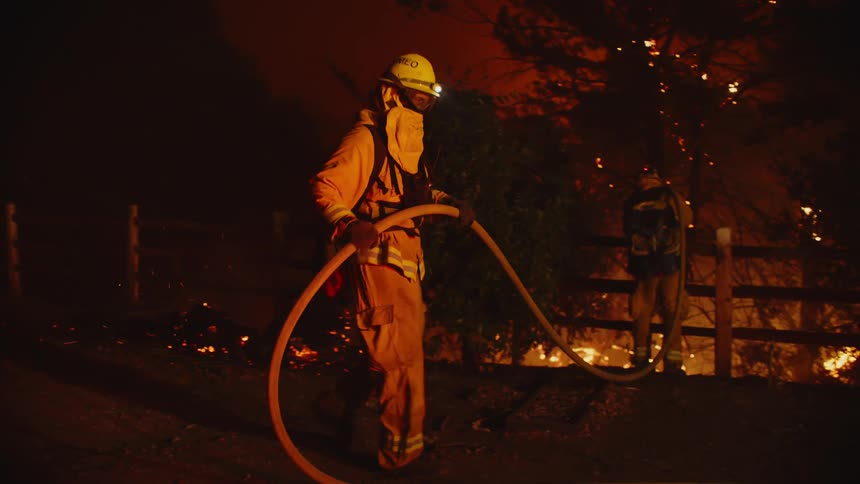 Firefighters carry a hose as they spray flames during a fire