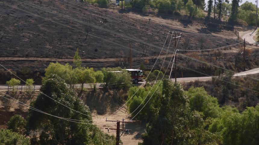 A fire truck slowly drives down a rural road through sloping hills and trees
