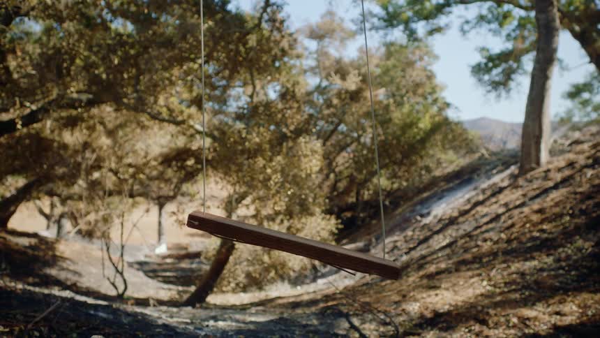 Wooden swing sways slightly near slope with mountains in the background
