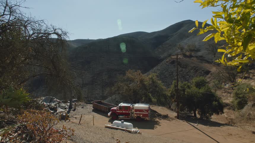 A firetruck parked near a dumpster parked on a road as a person walks away from the truck