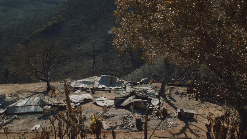 Firefighter walks through disaster debris near burnt mountain side