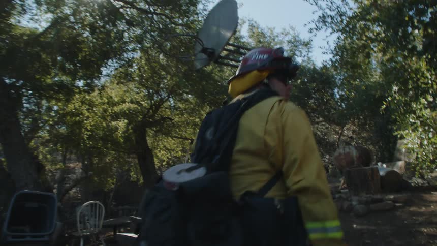 A firefighter walks around a home and property to assess the area on a sunny day