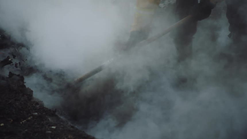 Smoke rolling off the ground as a person rakes the dirt