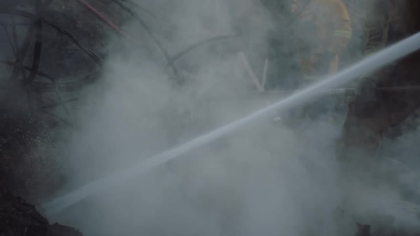 Firefighters wearing yellow protective gear spraying the burned ground on a hill with a hose