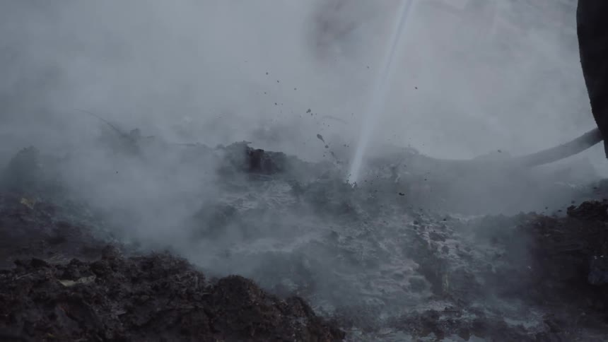 A firefighter spraying the ground creating mud as steam rolls off the surface
