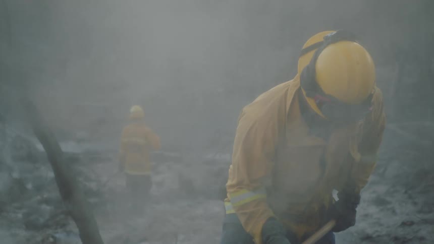 Firemen working around smokey grounds raking rubble