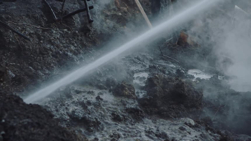 Fast stream of water sprays onto charred smoky ground creating sludge