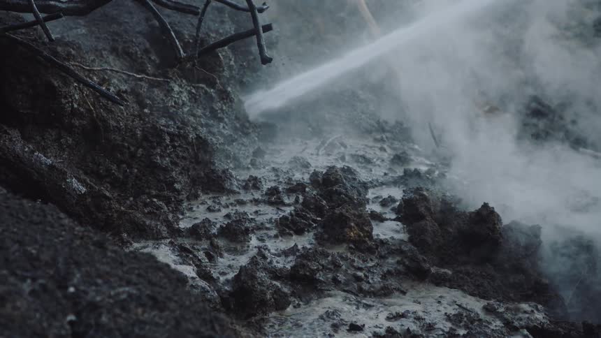 A hose being sprayed on muddy soil is it steams off the surface