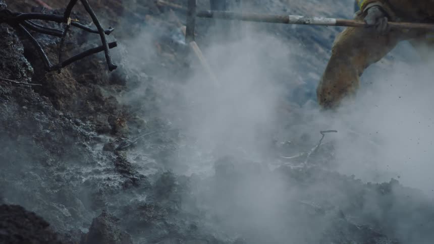 Firefighters dig and water smoking ground on slope