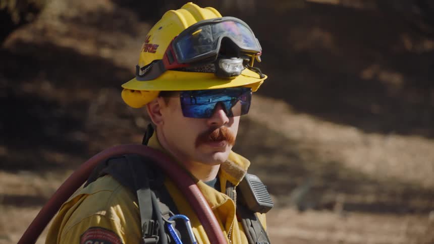 A fireman standing looking around wearing a helmet and a hose over one shoulder