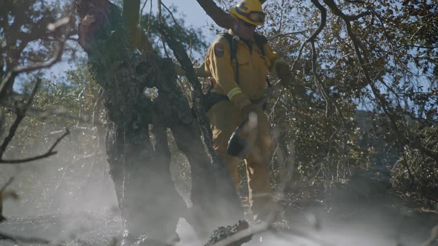 Firefighter using a shovel to dig in the ground as smoke billows from the ground