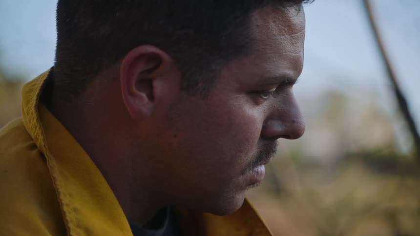 Close up of the face of a tired firefighter looking down while standing outdoors