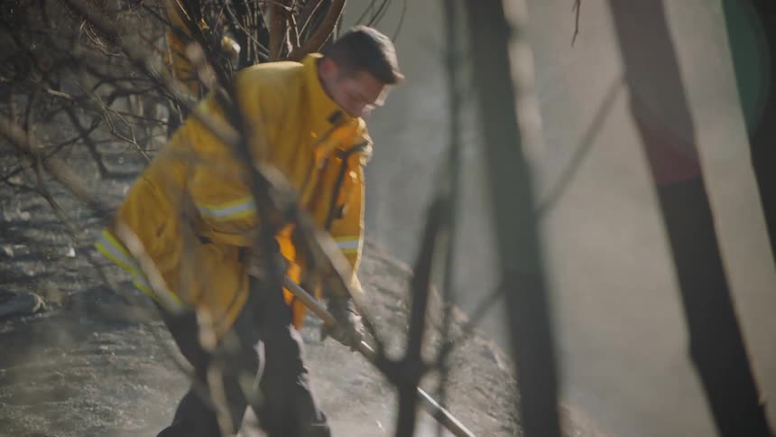 A fireman using a rake on smoking ground near a road