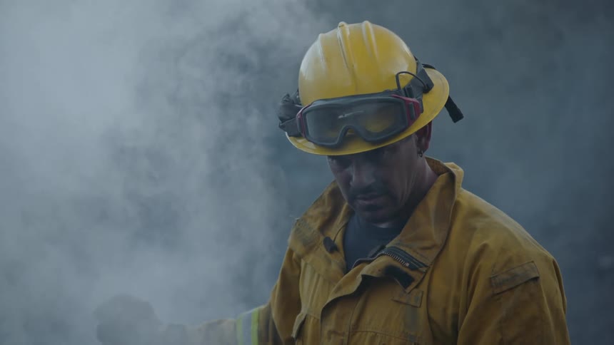 A firefighter is standing outside looking down as smoke fills the air around him