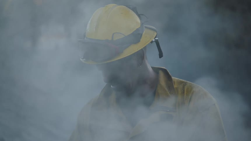 Smoke blows in a firemans face while standing in the woods