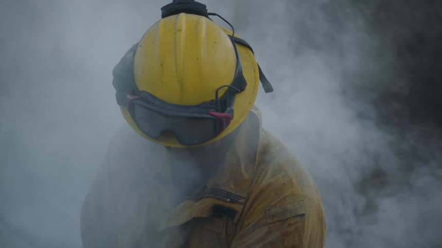 A firefighter is standing outside looking down as smoke fills the air around him