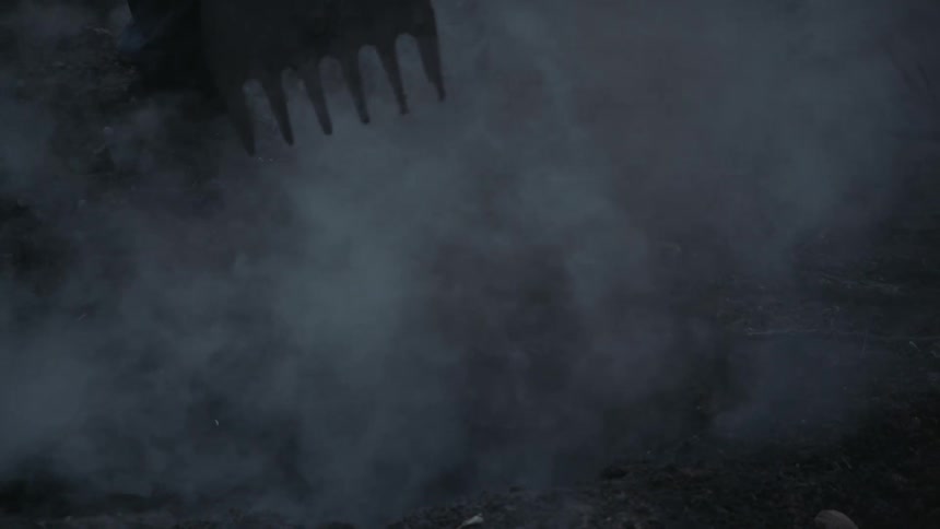A person using a rake on the round as fog and smoke roll over the ground