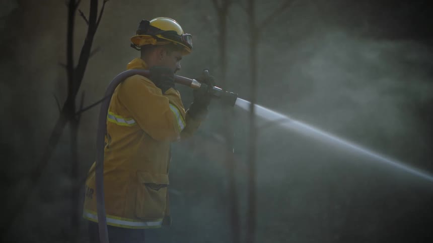 A firefighter using a hose to spray at the ground around him