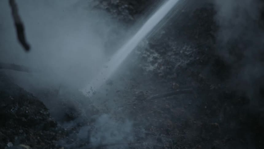 A fire hose putting out a strong stream of water and extinguishing whats left of a forest fire