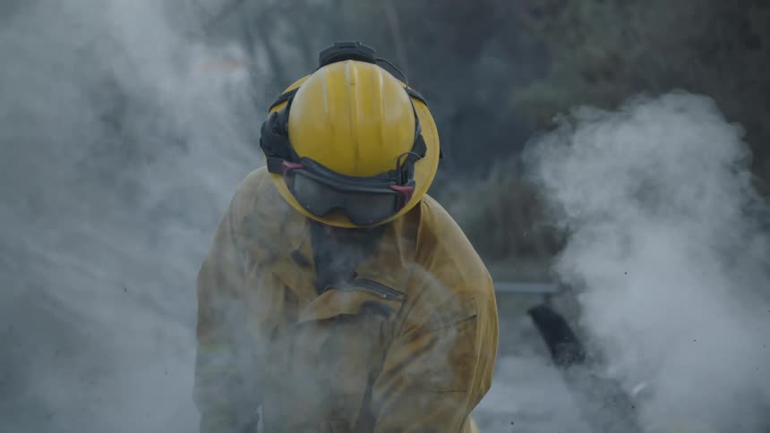 Firefighters stand outdoors as smoke rises from the ground