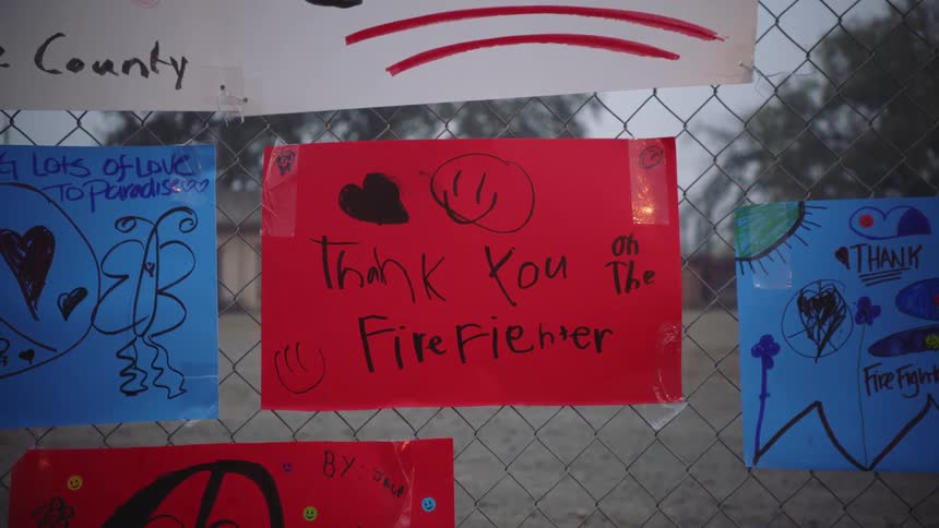 A fence in front of a schoolyard with handmade multicolored signs with words thanking the local firefighters
