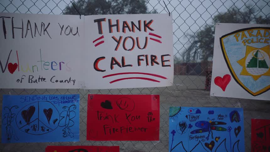Multiple posters attached to a chain link fence express thanks to firefighters