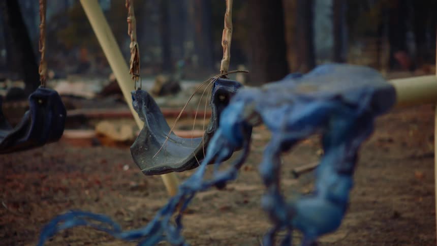 Close up of a swing set on the backyard of a burned down house