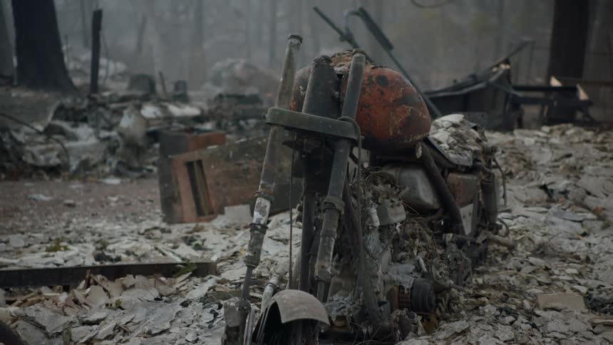 A pile of ashes and a burnt motorcycle among other debris and rubble