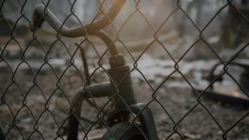 Close up of burnt tricycles near a wired fence in the forest at evening