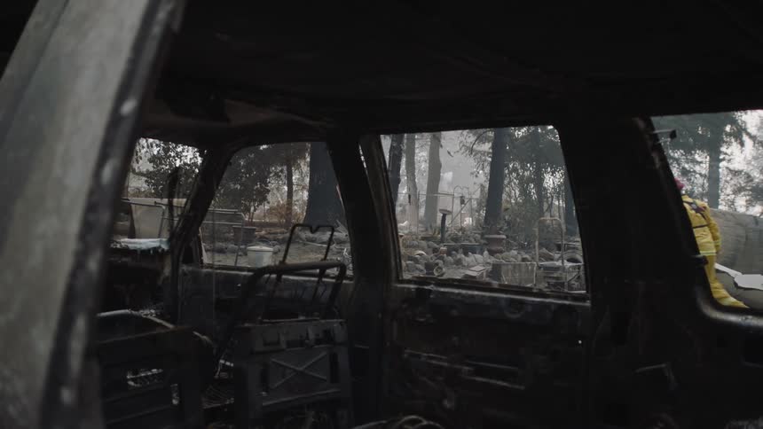The inside of a burnt vehicle as a firefighter walks by on the road