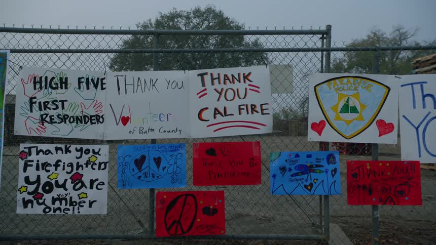 A collage of posters are attached to a metal fence in appreciation of california firefighters